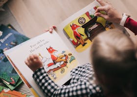 A child and adult reading an illustrated storybook together in a cozy setting.